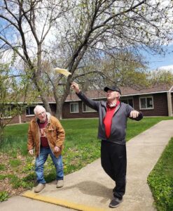 Two participants flying a paper airplane on a nice day outside at Breath of Life Adult Day Service.