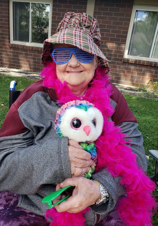 Breath of Life Participant on fun dress up theme day wearing. a pink boa outside holding an owl and wearing a hat and glasses!